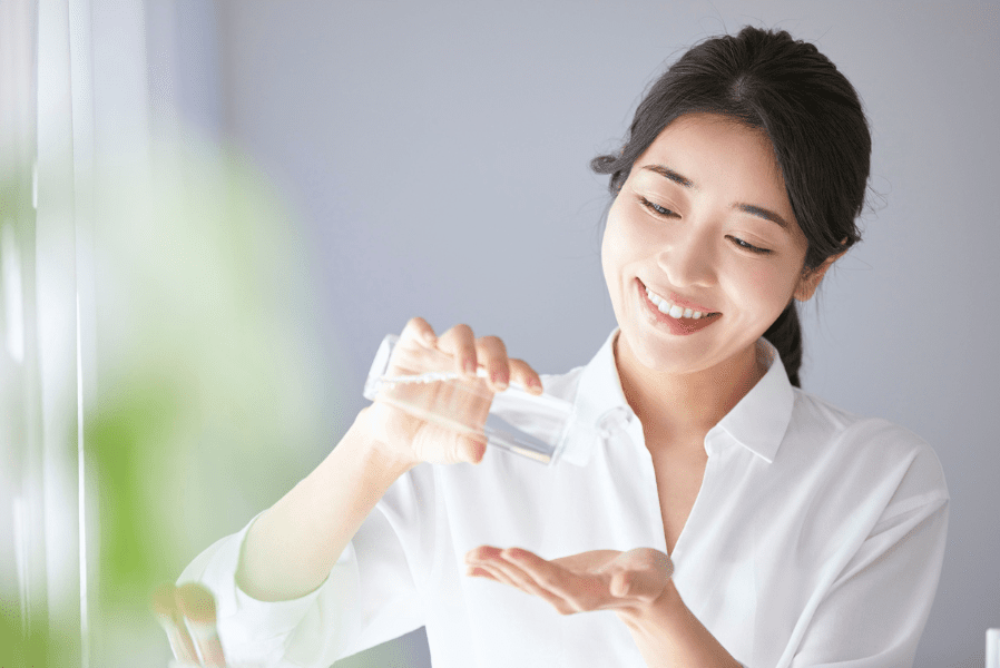 朝の光が差し込む明るい部屋で、女性が満足そうに微笑みながらスキンケアをしている様子｜アーバンコスメ