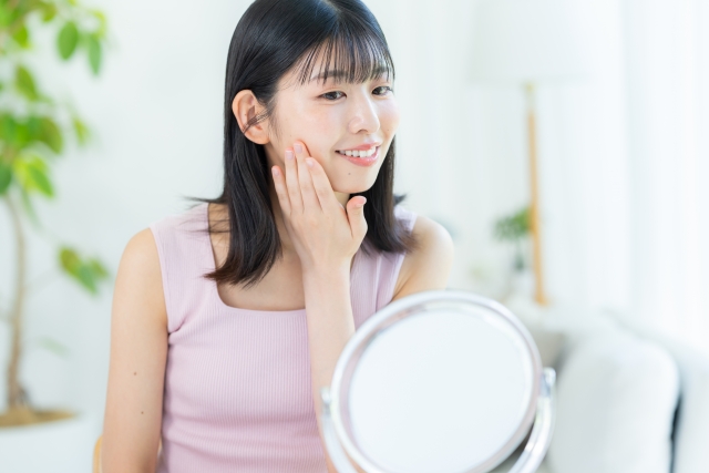朝の光が差し込む明るい部屋で、女性が鏡の前で、満足そうに肌のハリや調子を確かめている様子｜アーバンコスメ