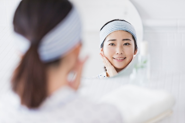 女性が鏡の前で、満足そうに微笑みながら、肌のツヤやハリなどを確かめている様子