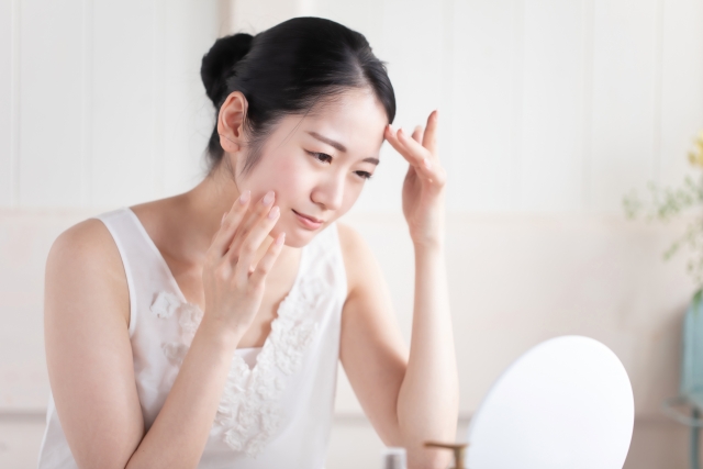 卓上の鏡を覗き込み、季節の変わり目による肌荒れや赤みの広がりを心配そうにチェックしている女性の様子