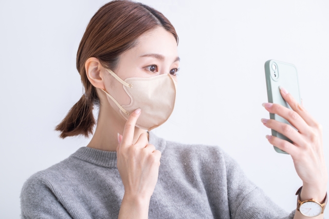 マスクをした女性がスマートフォンのインカメラを使い、季節の変わり目による肌荒れや乾燥の症状をチェックしている様子