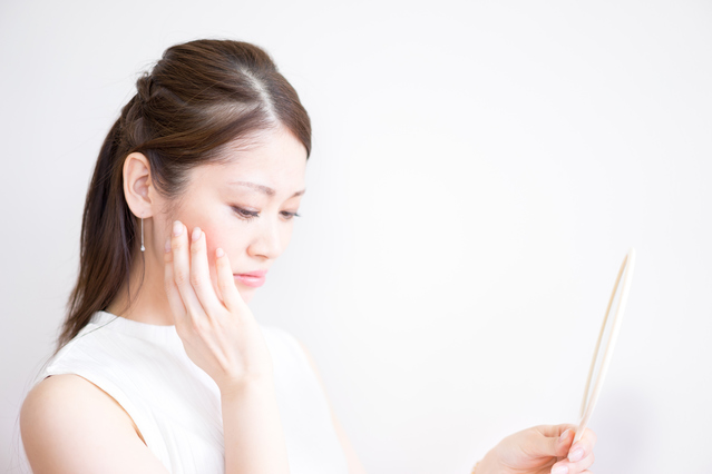 手鏡で肌の状態をじっくりと確認し、花粉シーズンの肌荒れや赤みに悩む女性の様子｜アーバンコスメ