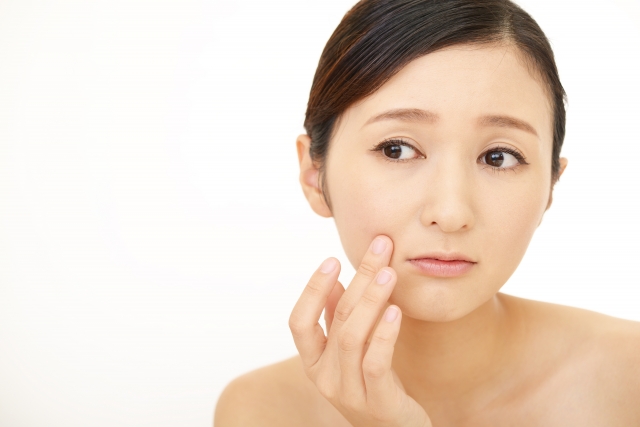 鏡を覗き込み、50代・60代特有の小鼻の黒ずみや頬の毛穴の開きを指で触れながら、春の肌変化を心配そうにチェックしている女性の様子