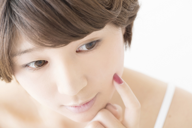 指先でそっと自身の頬に触れ、肌の弾力やコンディションを確かめながら、ケアに満足している、明るく清潔感のある女性の様子｜アーバンコスメ