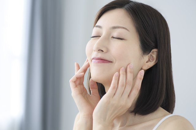 スキンケア後の肌の仕上がりに自信を感じ、晴れやかな表情で潤いあふれる素肌の質感を確かめている女性の様子｜アーバンコスメ