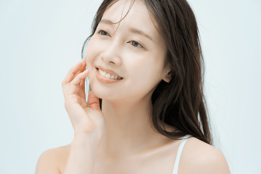 春の明るい陽光の下、柔らかな光に包まれながら、自身の肌の質感や化粧ノリの変化にポジティブな期待を寄せて、穏やかに微笑んでいる女性の様子｜アーバンコスメ